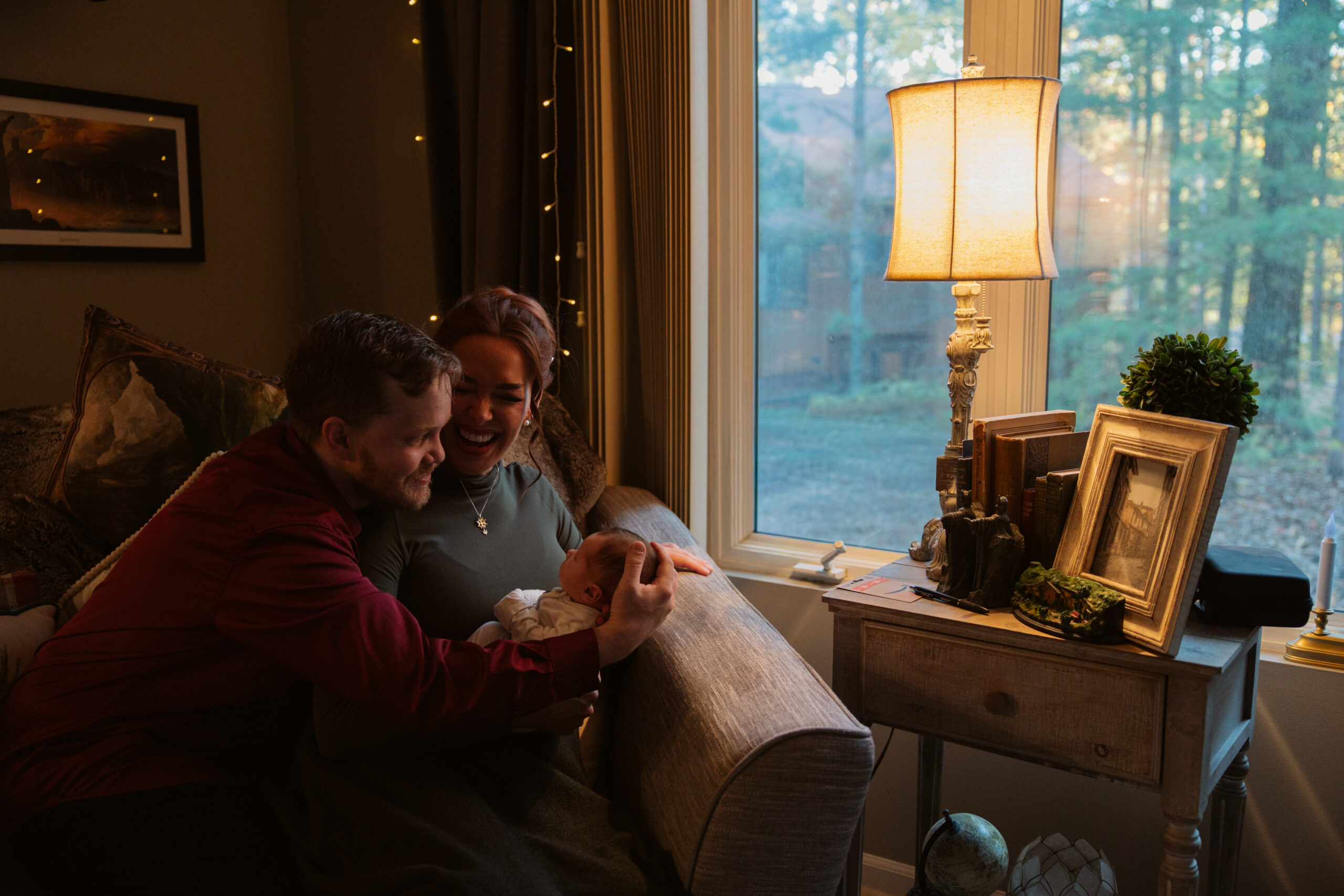 Husband and wife holding baby in living room during newborn photos in traverse city. Photo by Traverse City Photographer Lina Lavonne Photography