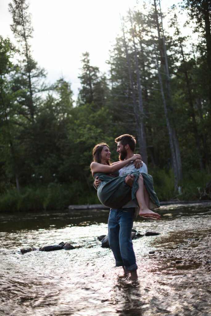 man carrying woman through river during engagement photos in traverse city michgian photographer