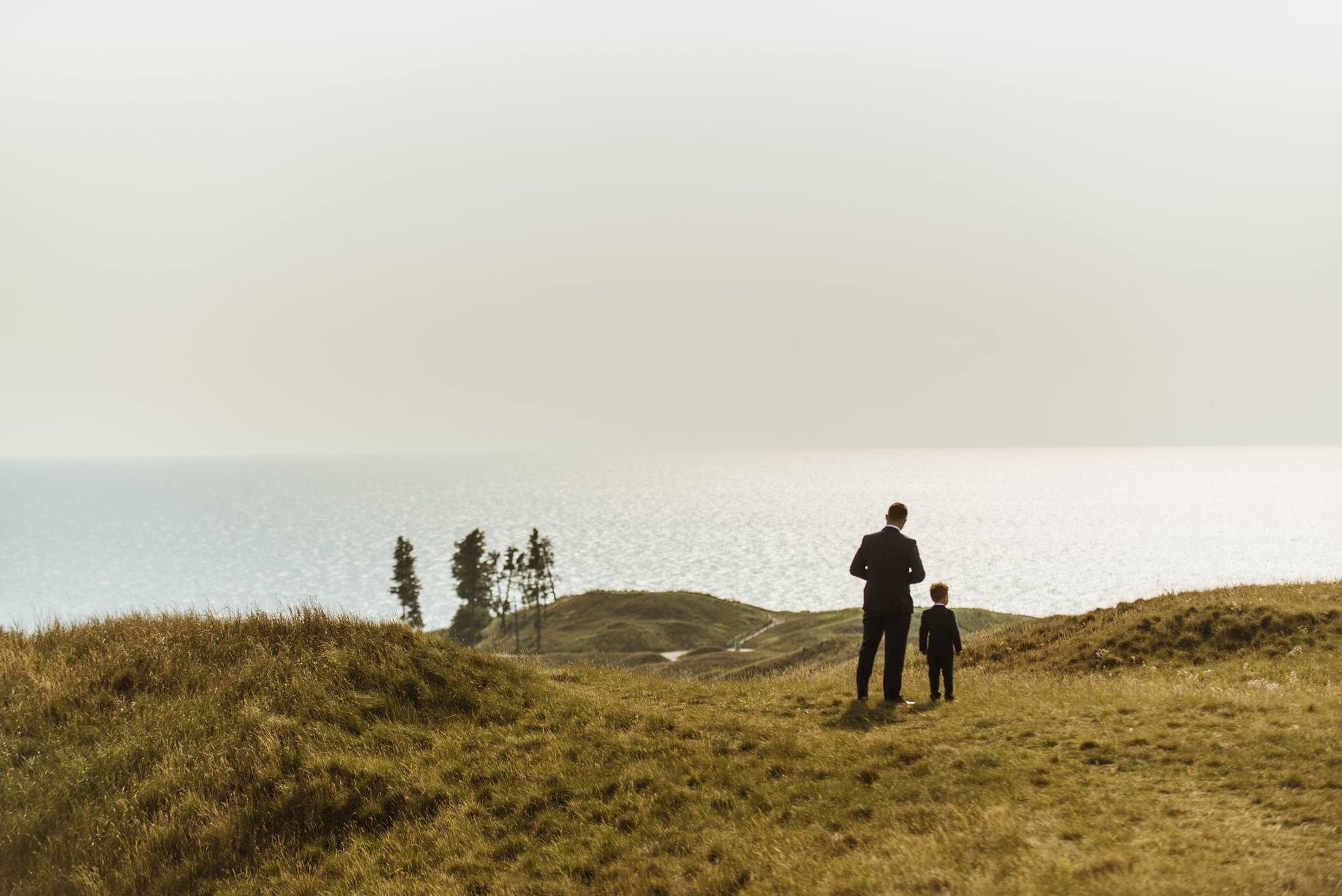 groom and son standing on rolling hills on lake michigan in arcadia bluffs