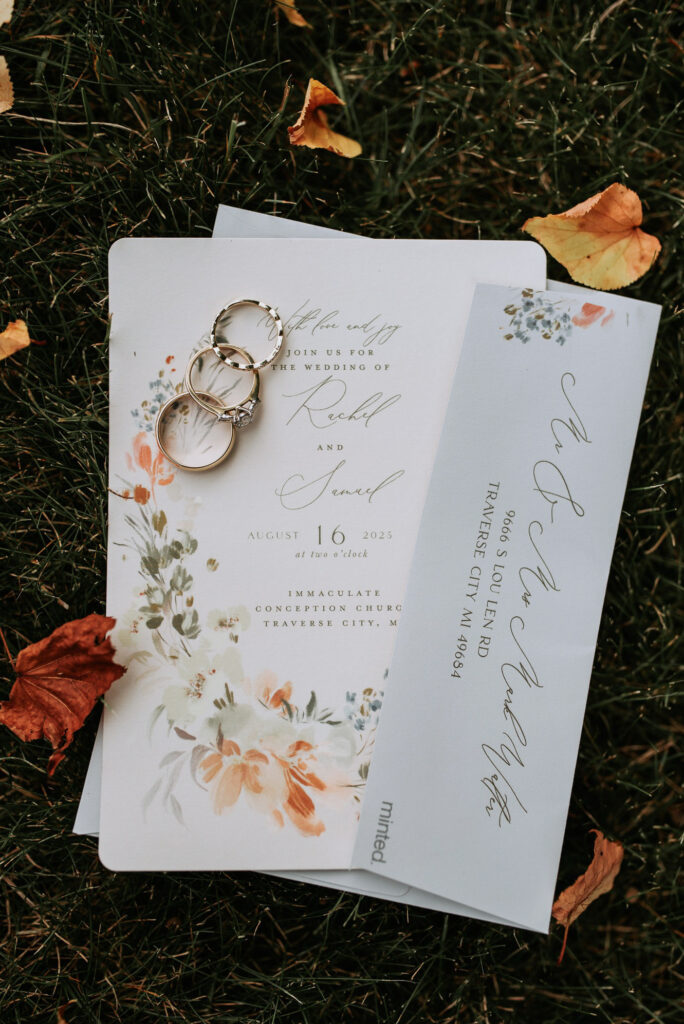 wedding invitations and rings sitting in the grass at private home in northern michigan. Photo by traverse city wedding photographer lina lavonne photography