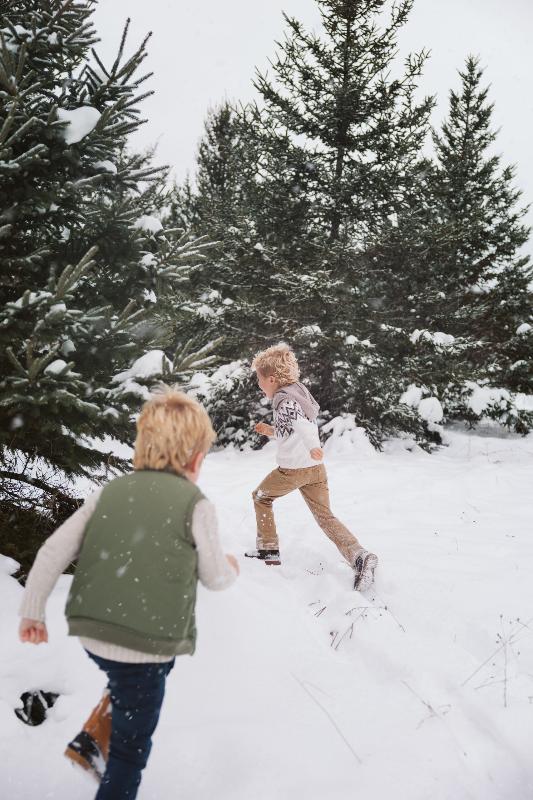 two boys running through snow during family portraits in northern michigan