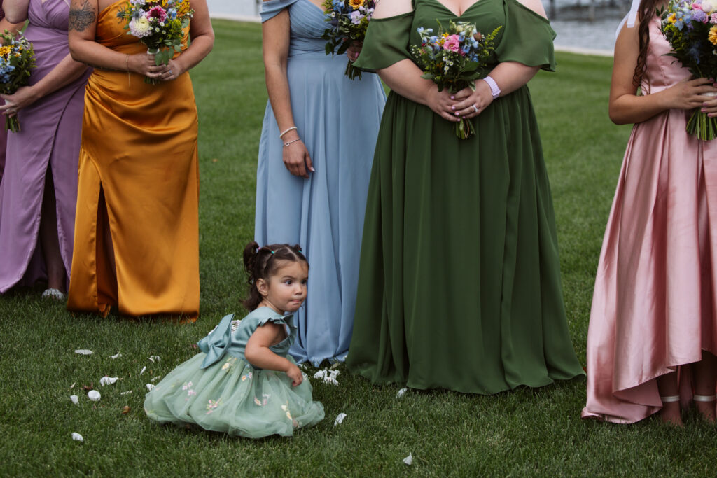 flower girl sitting next to bridesmaids feet at wedding in east jordan boathouse on lake charlevoix