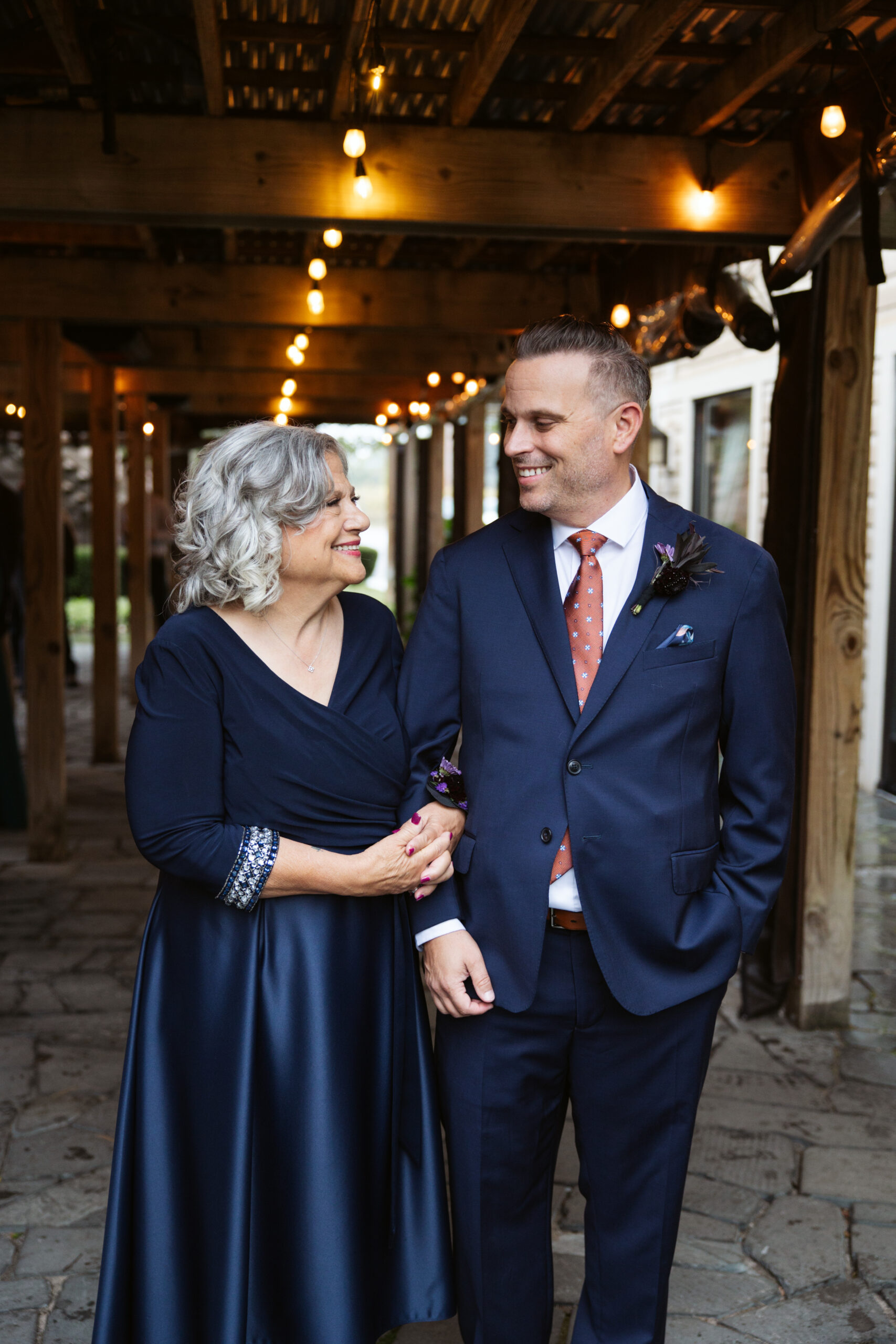 groom and his mother posing for pictures on a rainy day at peninsula cellars wedding photo by traverse city photographer
