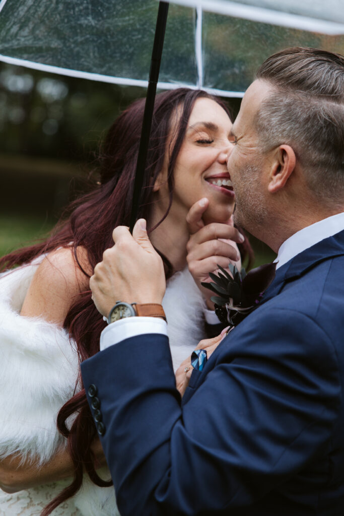 groom pulling his bride in for a kiss under an umbrella on old mission peninsula during a peninsula cellars wedding