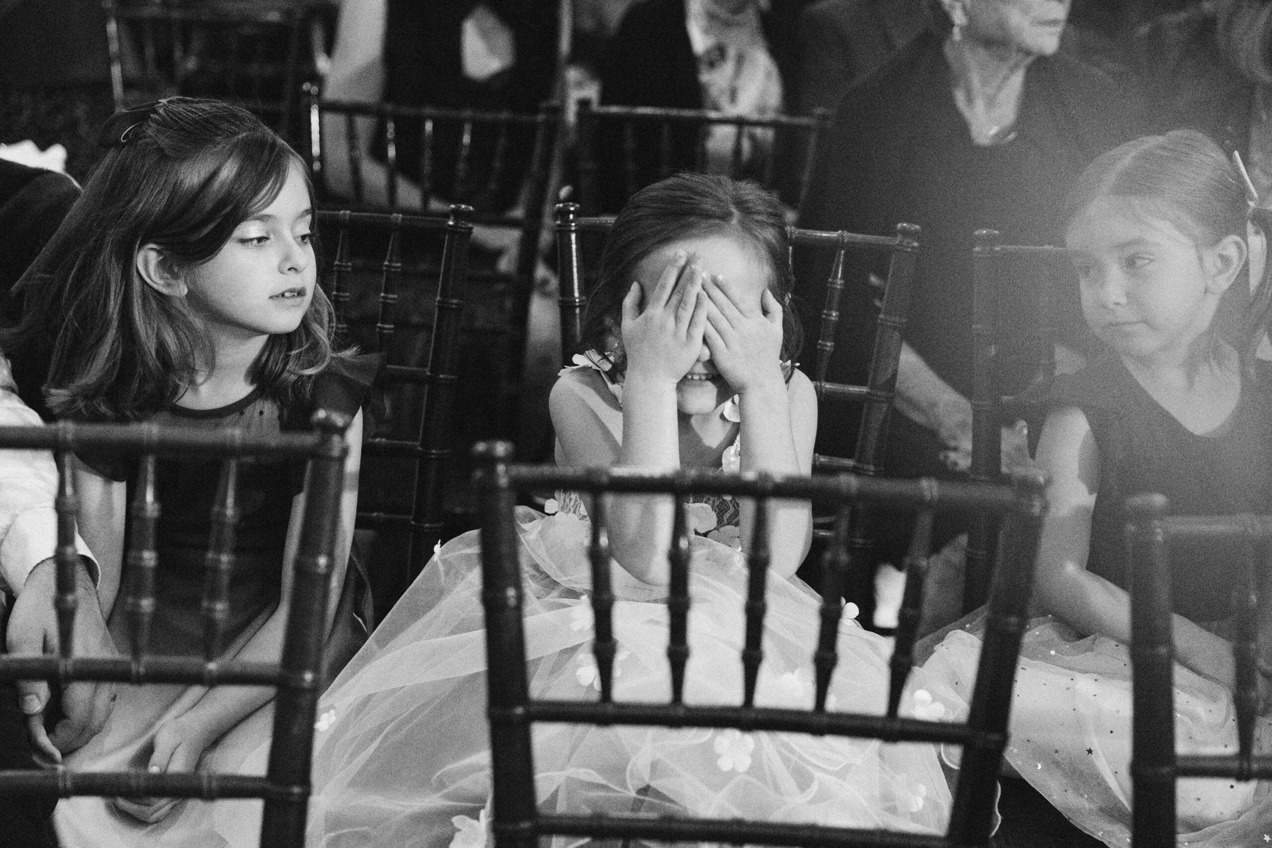 black and white image of flower girl sitting in a row of chairs at peninsula cellars wedding ceremony
