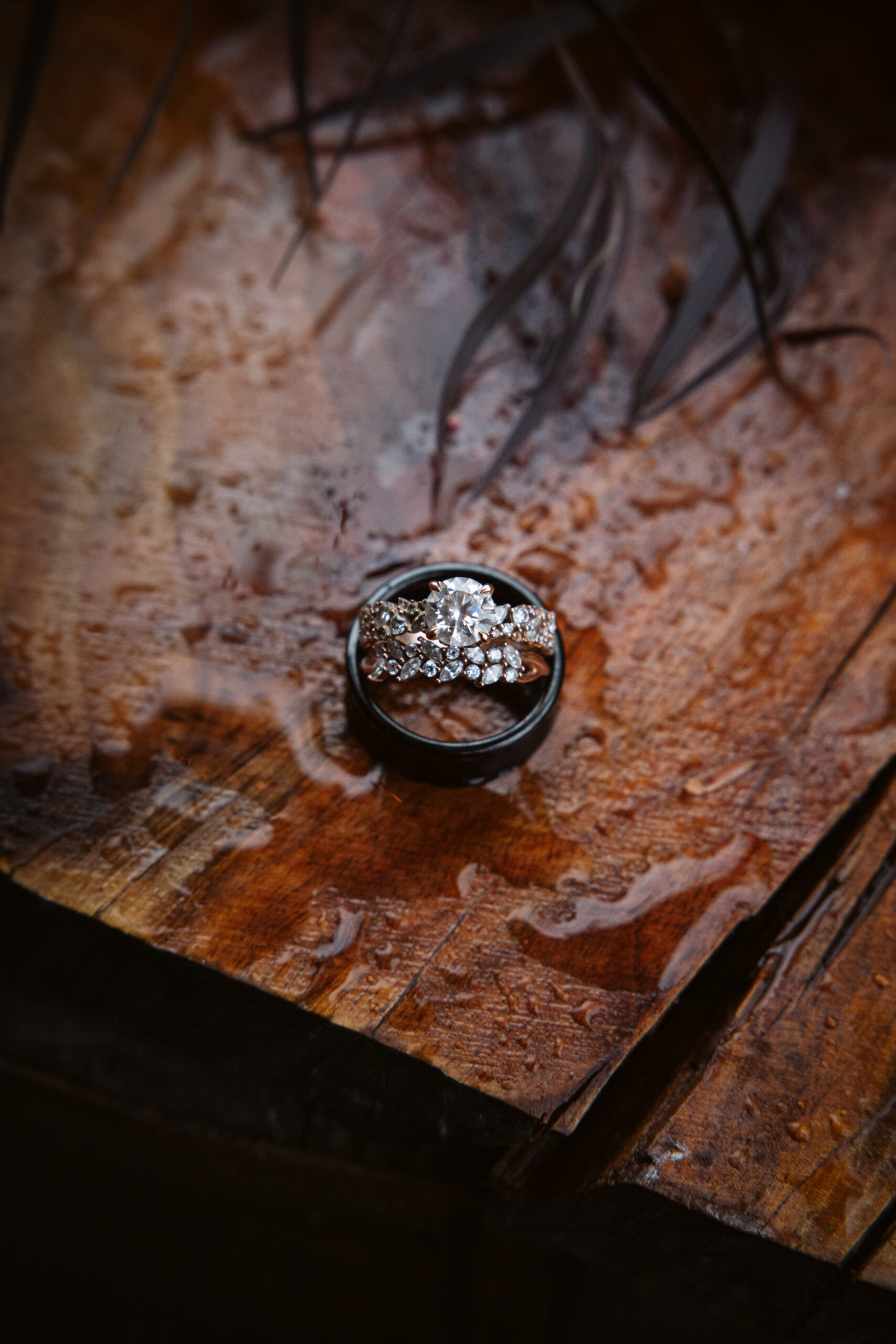 close up of wedding rings sitting on rain covered wood at peninsula cellars wedding in traverse city michigan