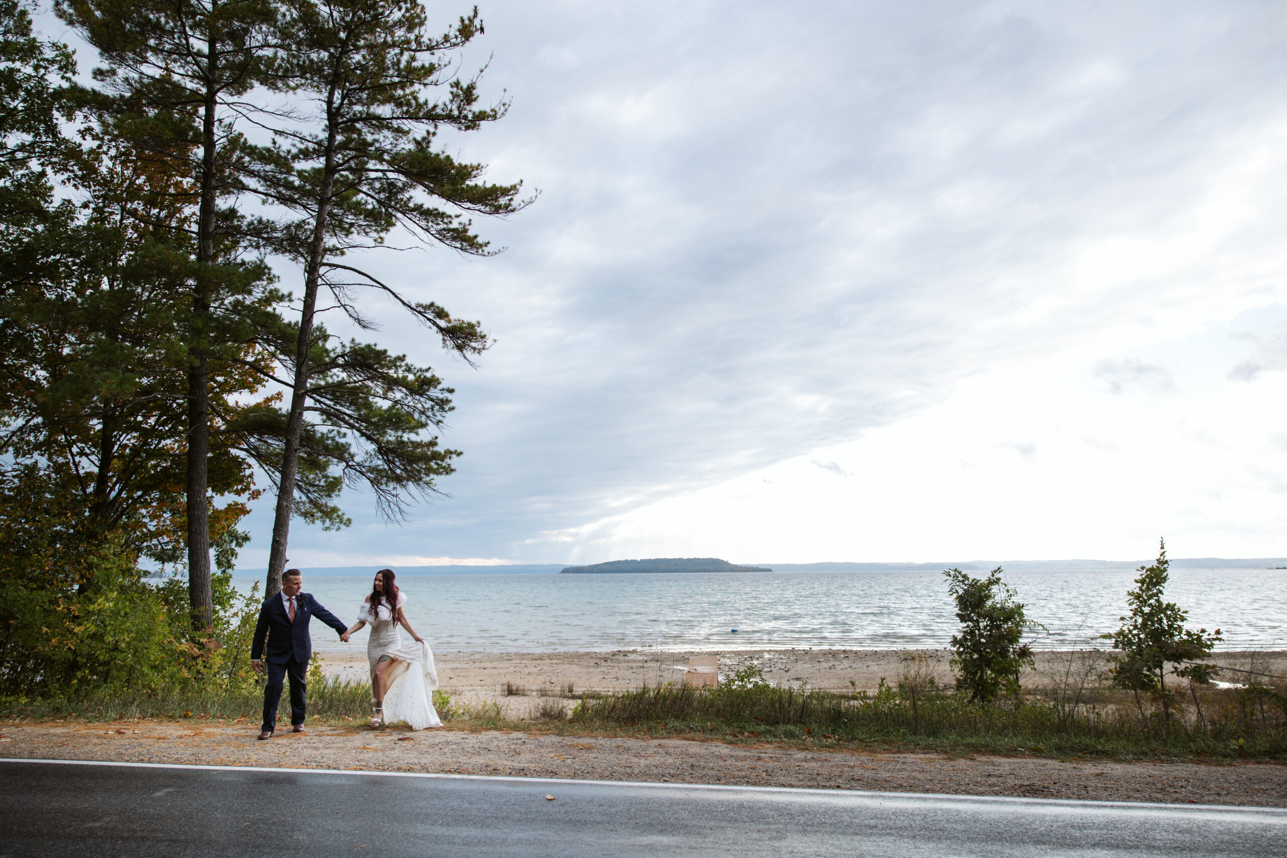 wide image of bride and groom walking across road at peninsula cellars wedding in traverse city michigan