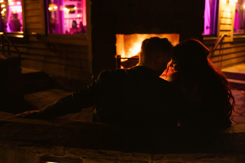 bride and groom sitting at the fireside backlit at night at peninsula cellars wedding in traverse city michigan