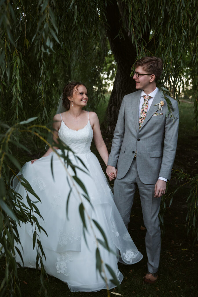 bride and groom walking through willow branches at starry night barn wedding in suttons bay michigan