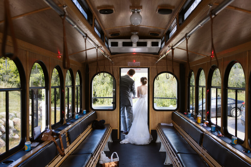 bride and groom standing on the back of a wedding trolly on their way to a reception in suttons bay