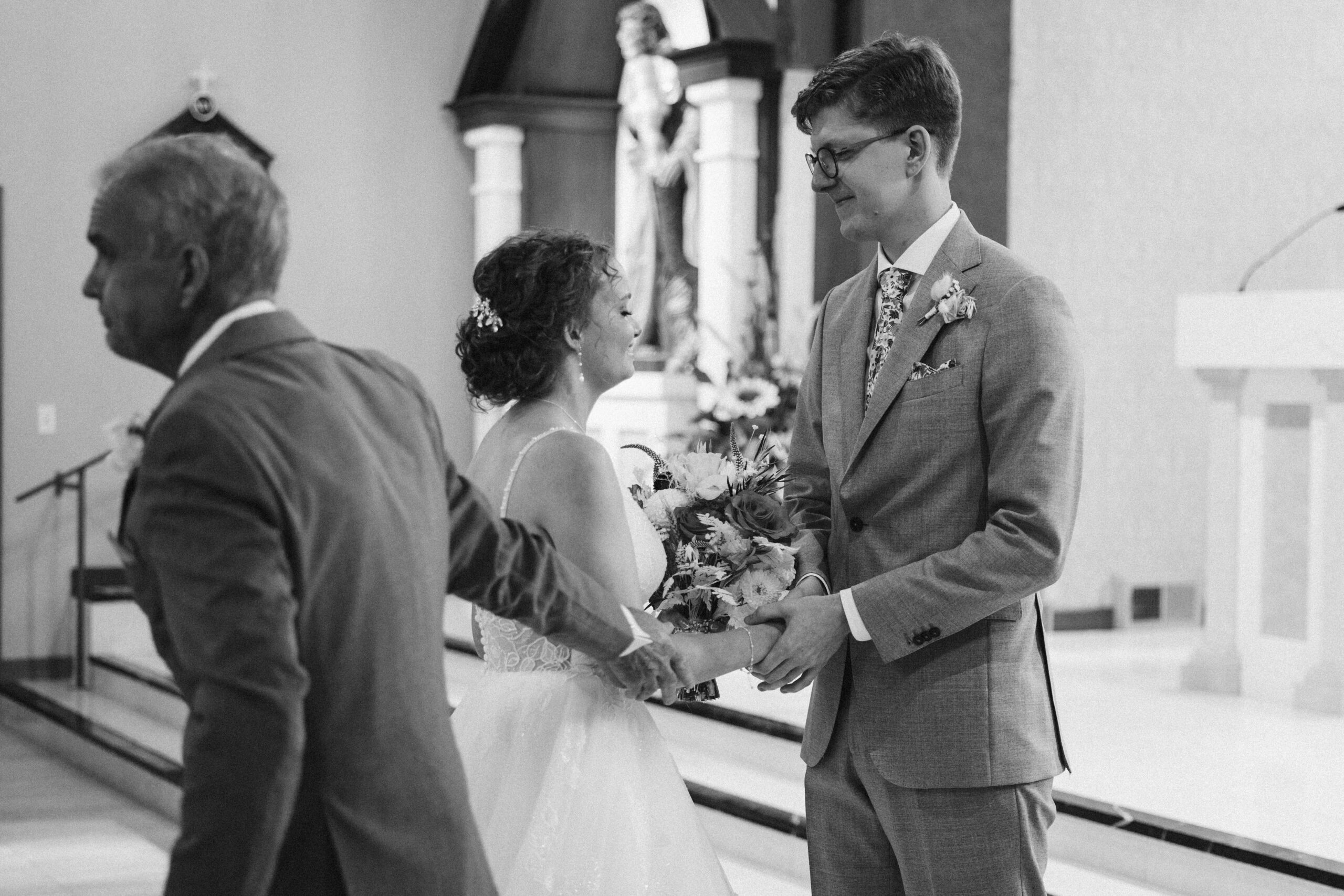brides father handing off the bride to the groom at immaculate conception in traverse city michigan