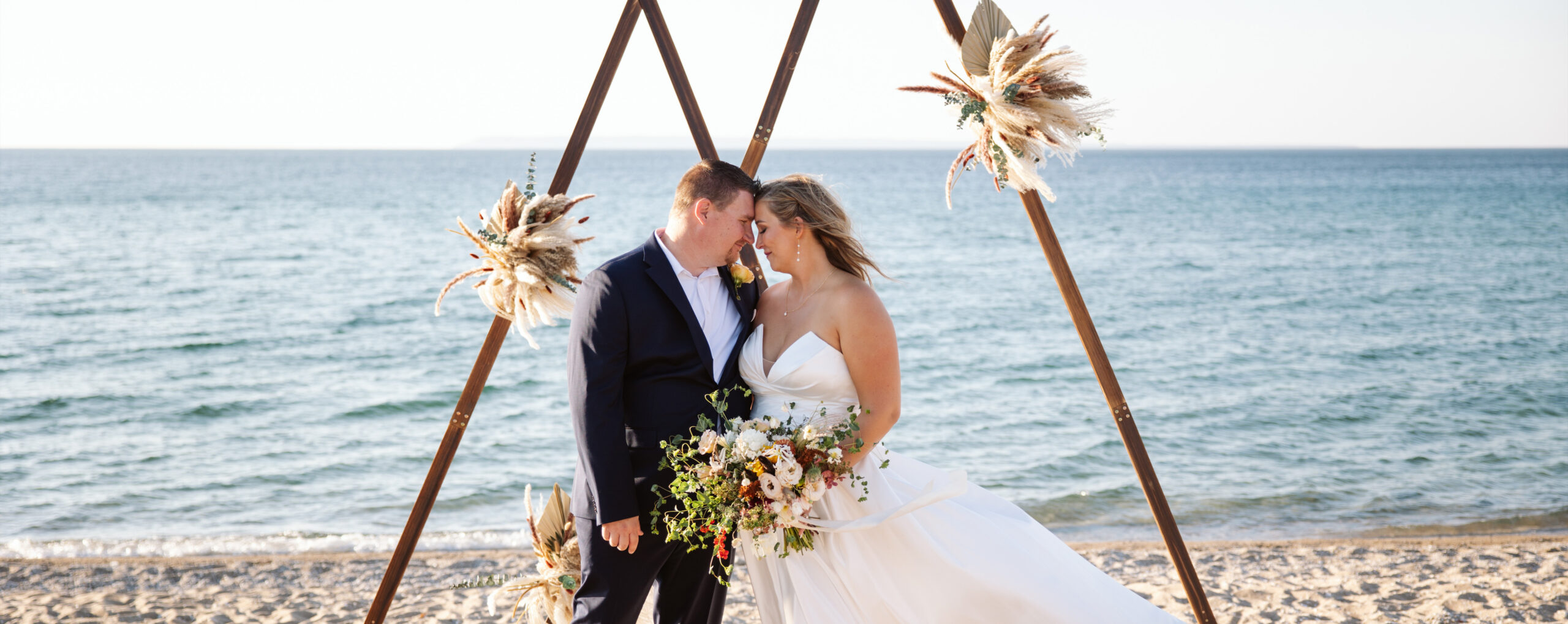 bride and groom standing next to arch on lake michigan beach during wedding in glen arbor michigan