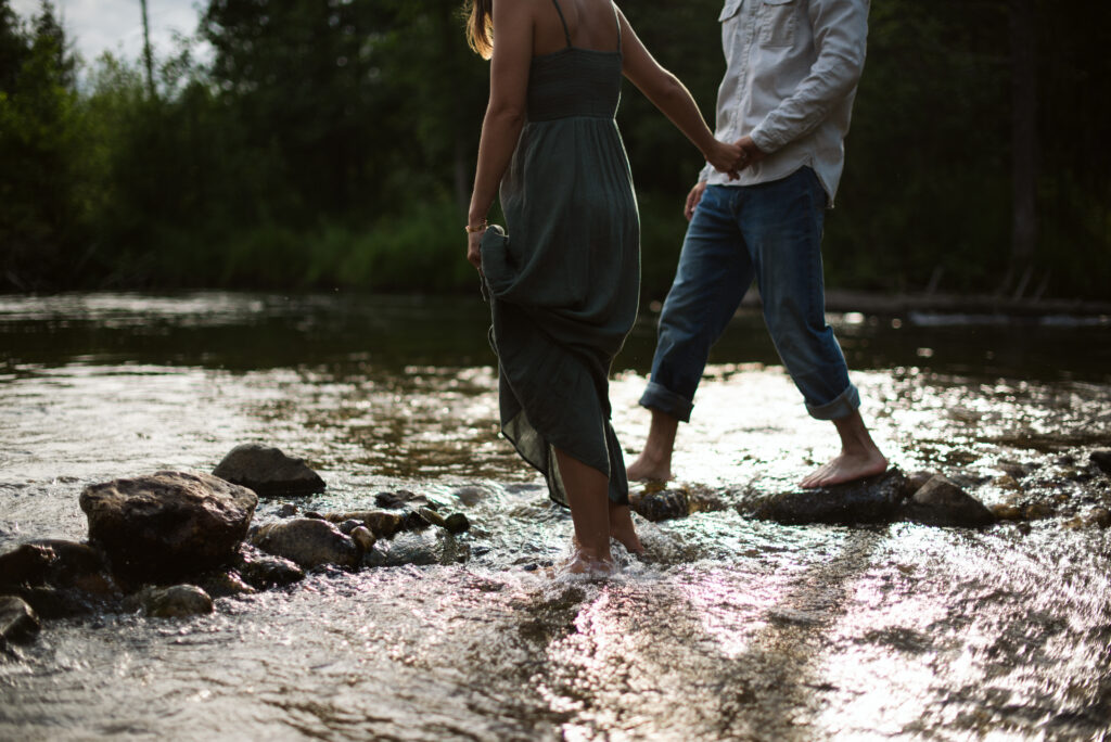 man and woman holding hands back lit in a river during engagement photos in traverse city