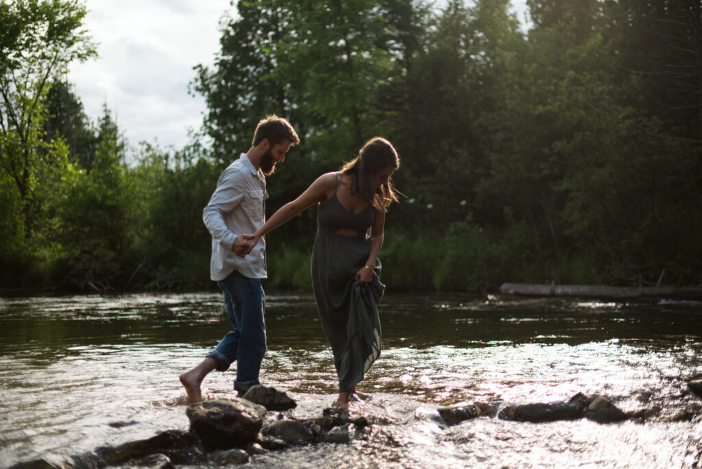 man and woman holding hands in the middle of the boardman river during traverse city engagement session