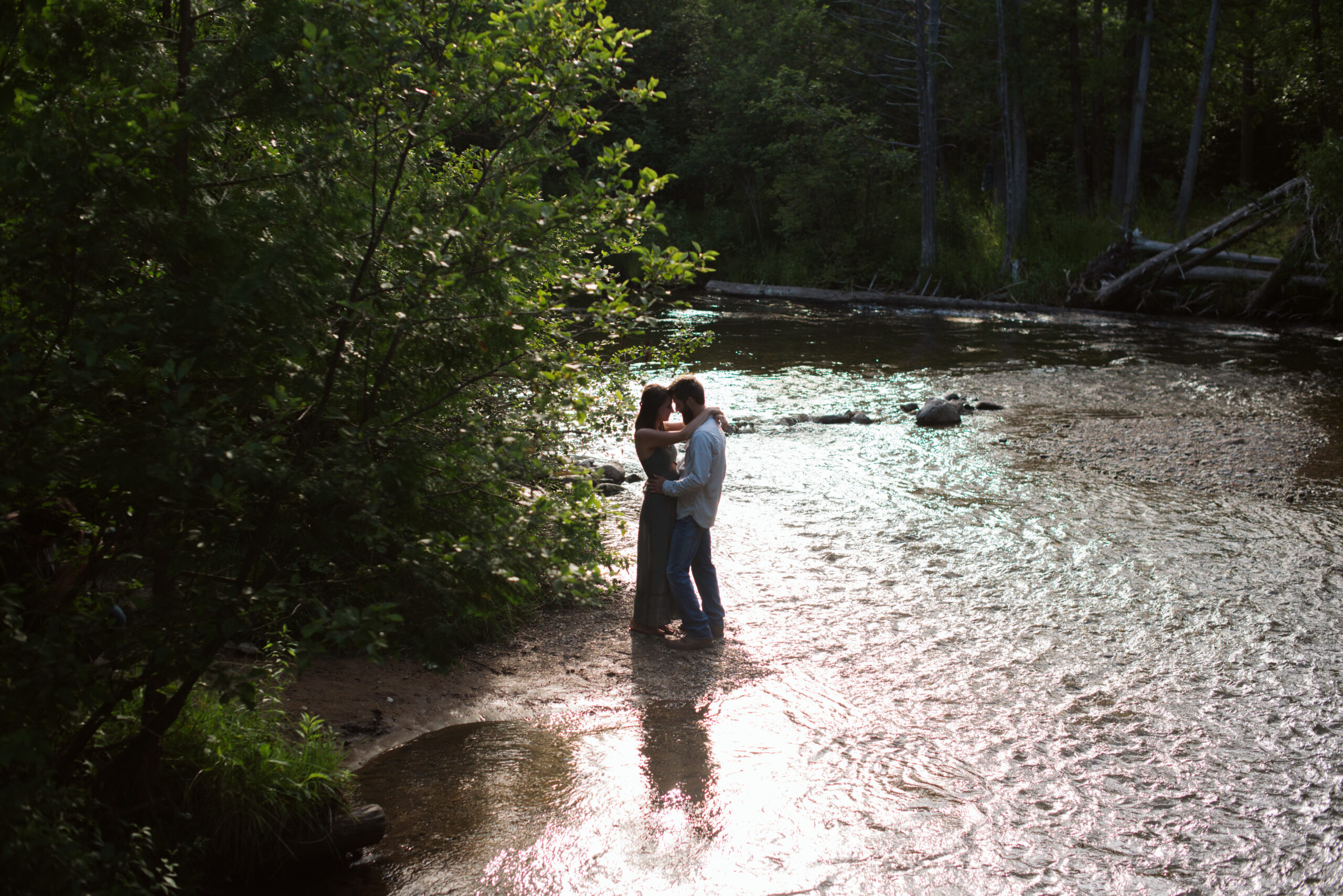 man and woman holding hands in the middle of the boardman river during traverse city engagement session