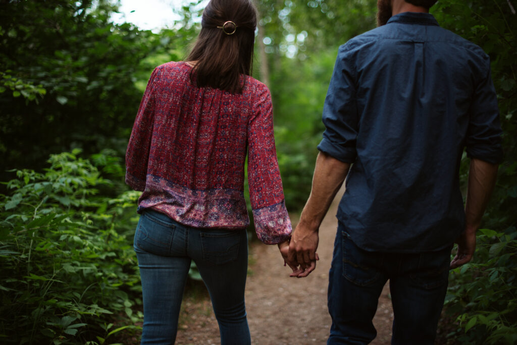man and woman holding hands walking through the woods during traverse city engagement session