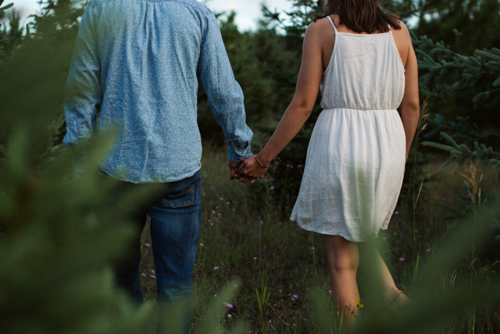 man and woman holding hands in a field during traverse city engagement session