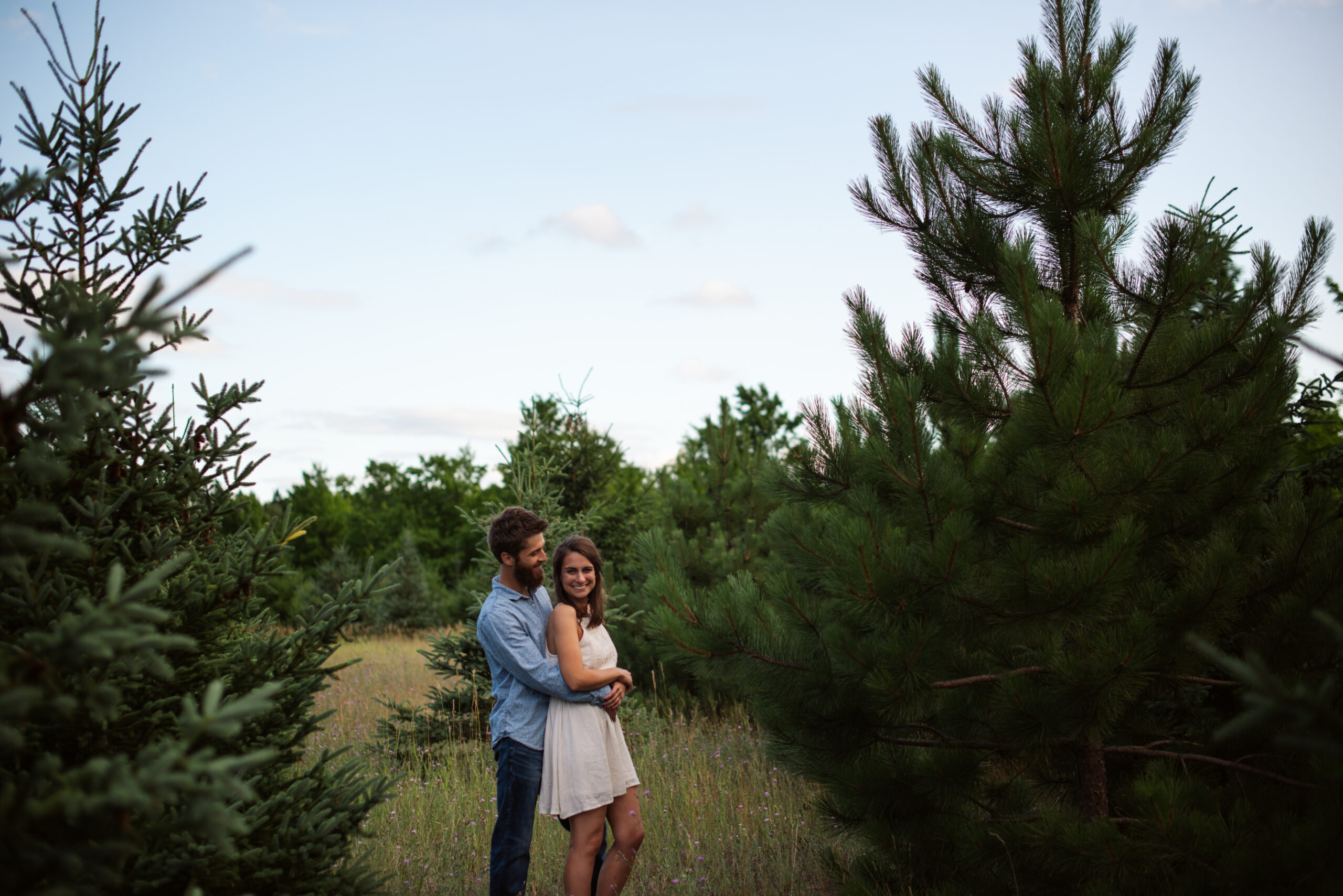 man holding bride in the middle of a field with trees during traverse city engagement session