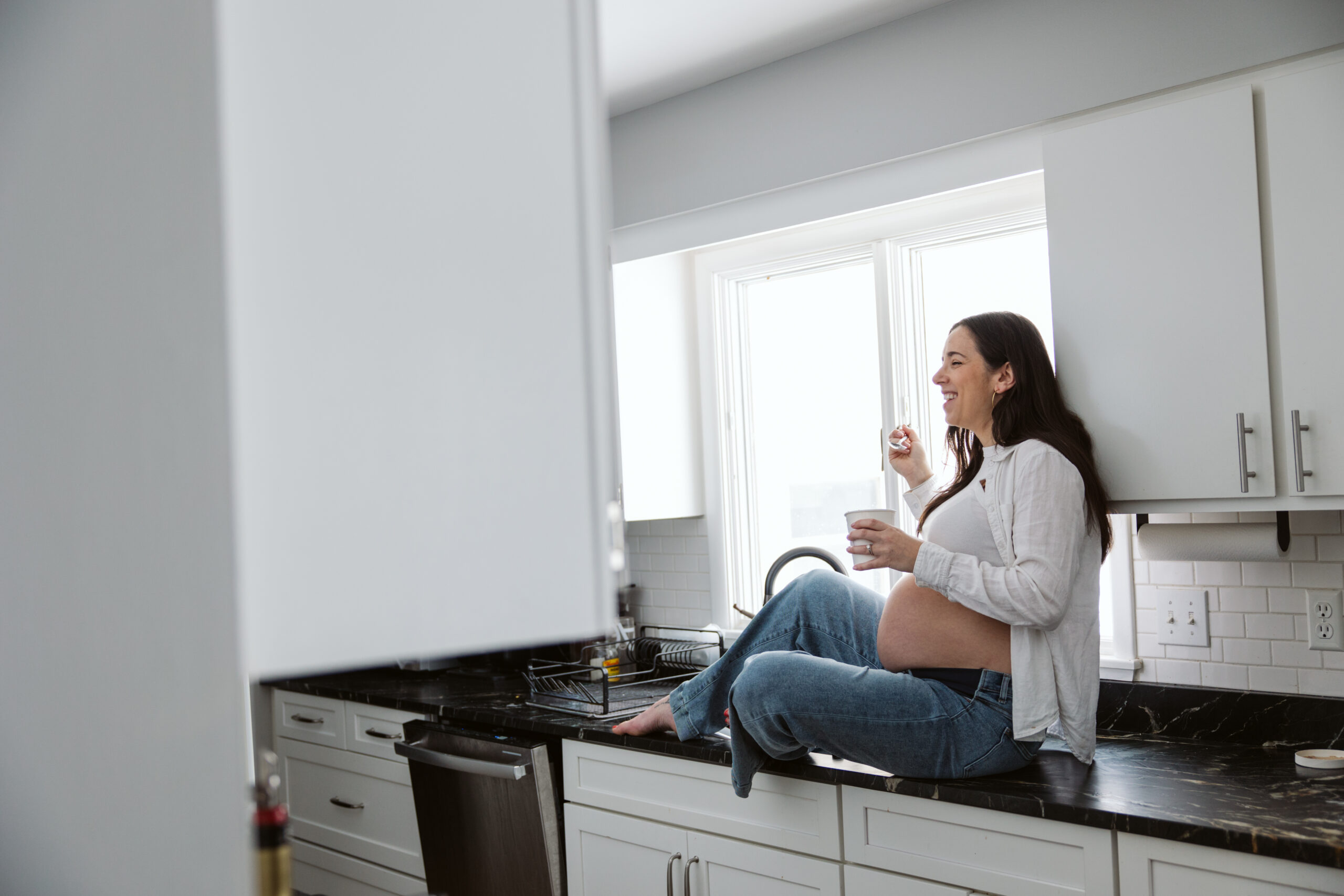 pregnant woman sitting on kitchen counter durning home maternity photos in traverse city michigan