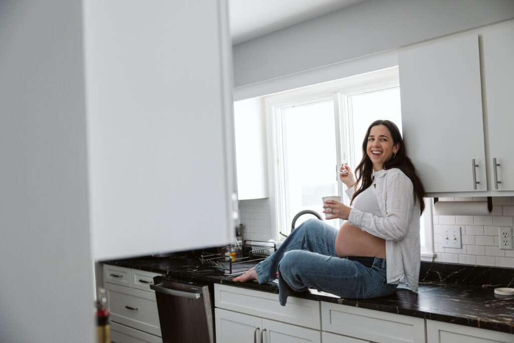 pregnant woman sitting on the counter in a kitchen during maternity photos in traverse city. 