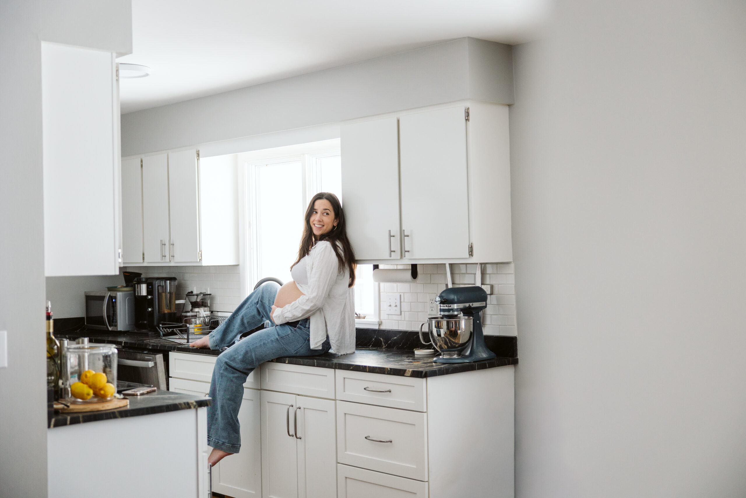 pregnant woman sitting on kitchen counter durning home family photos in traverse city michigan