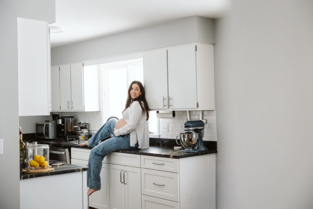 pregnant woman sitting on the counter in a kitchen during maternity photos in traverse city. 