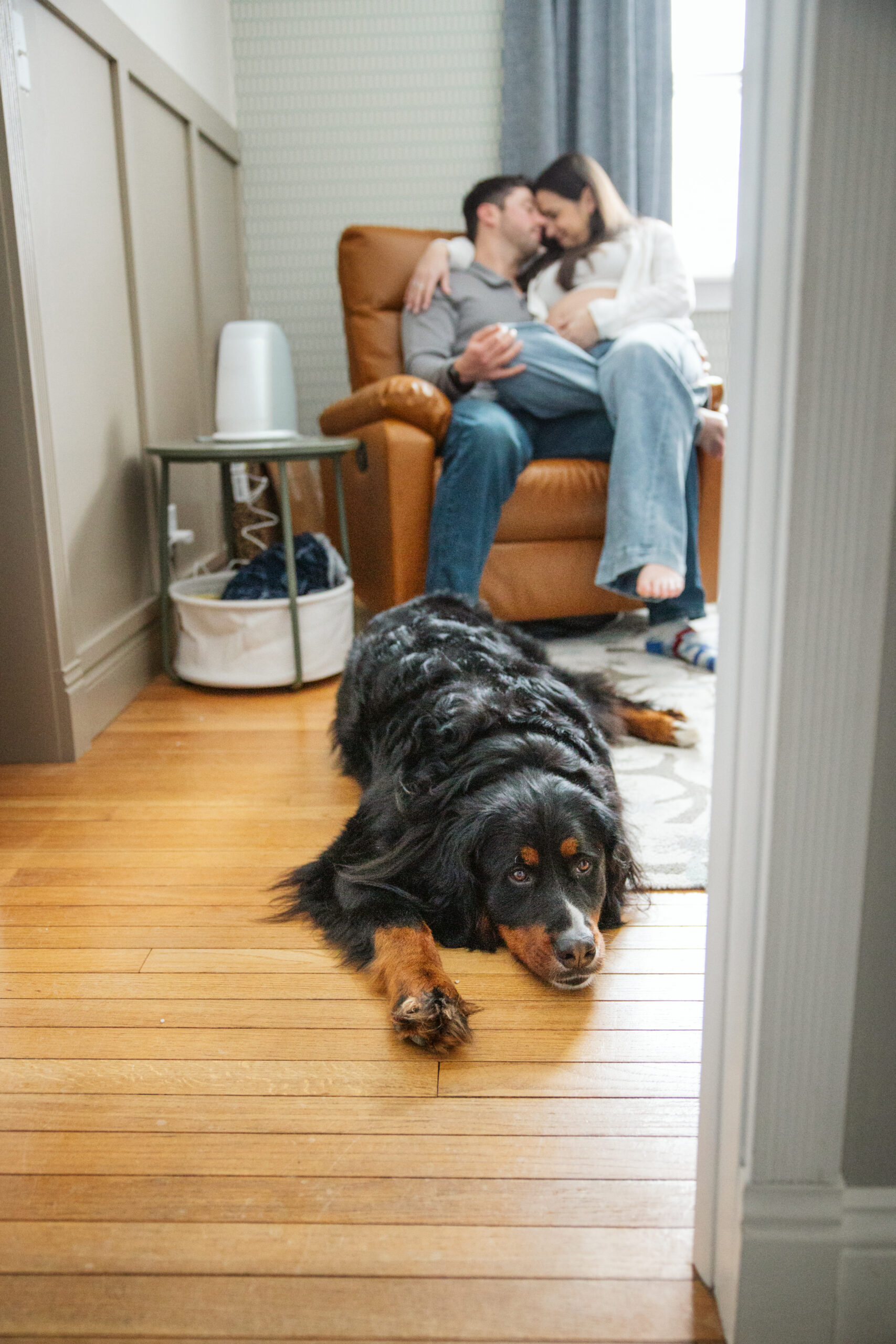 husband and wife sitting on a chair in nursery room with dog durning home family photos in traverse city michigan