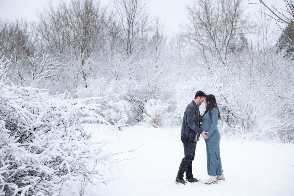 husband and wife standing in snow during maternity session in traverse city michigan