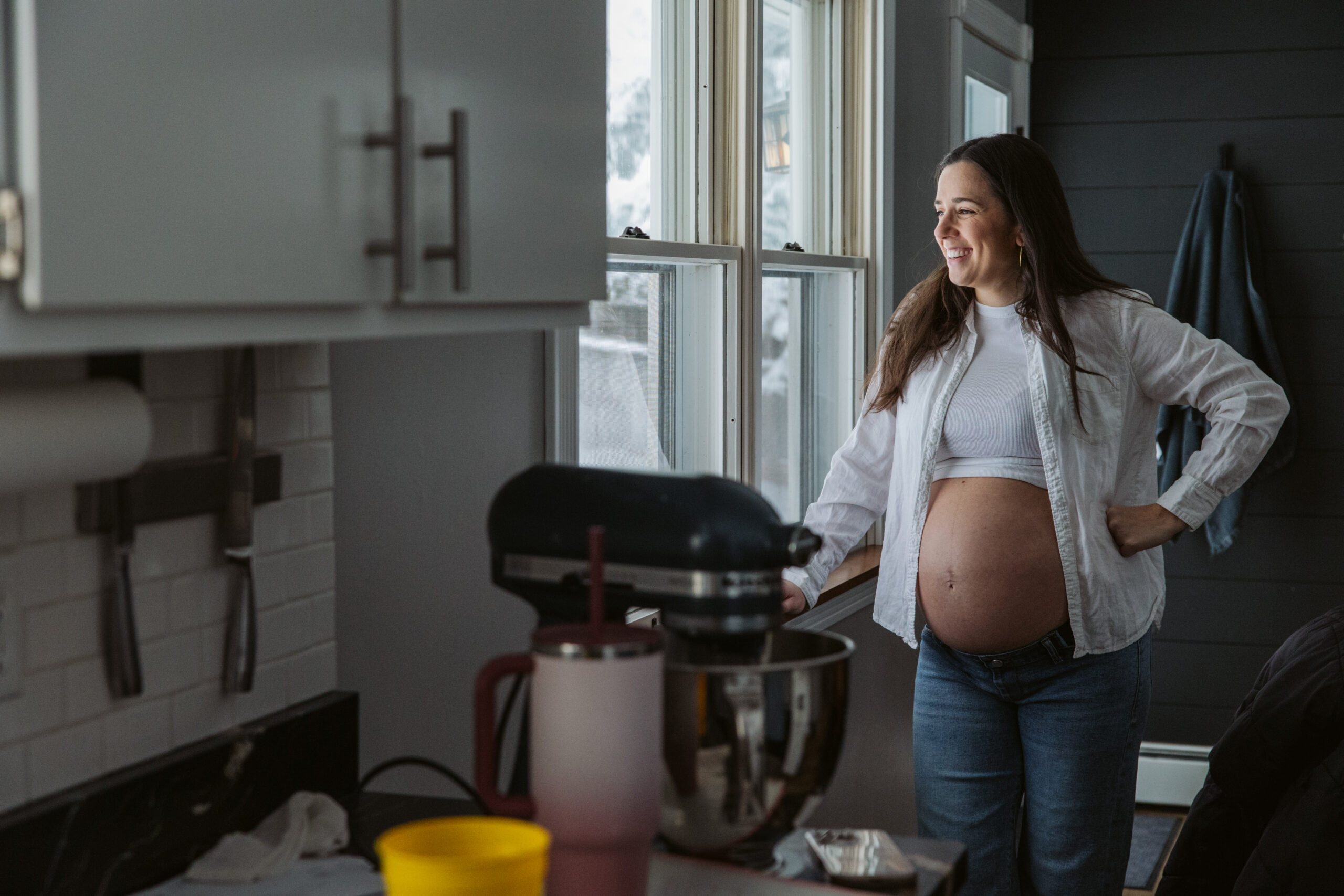pregnant woman standing at window durning home maternity photos in traverse city michigan