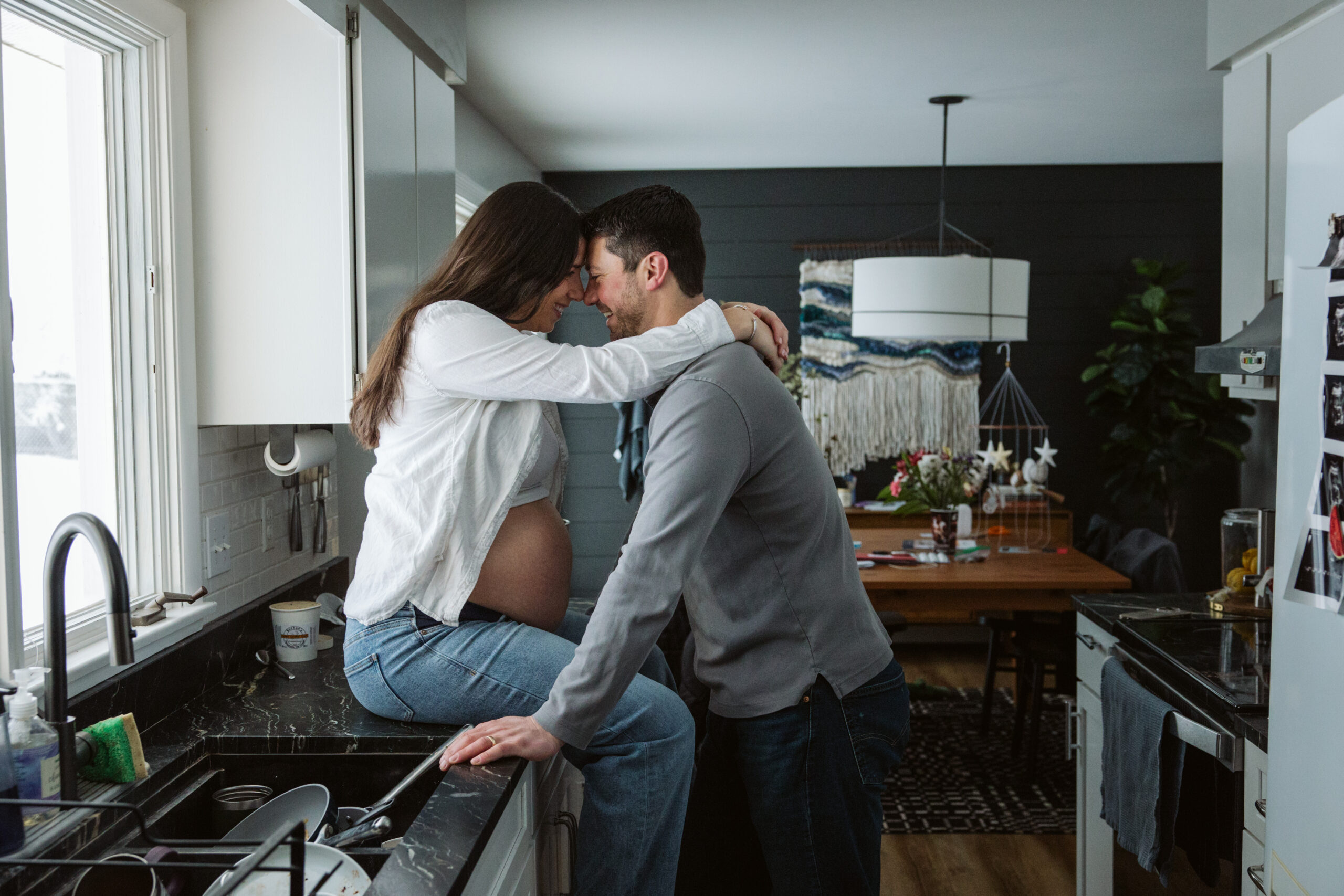 pregnant woman sitting on the counter in a kitchen during maternity photos in traverse city. 