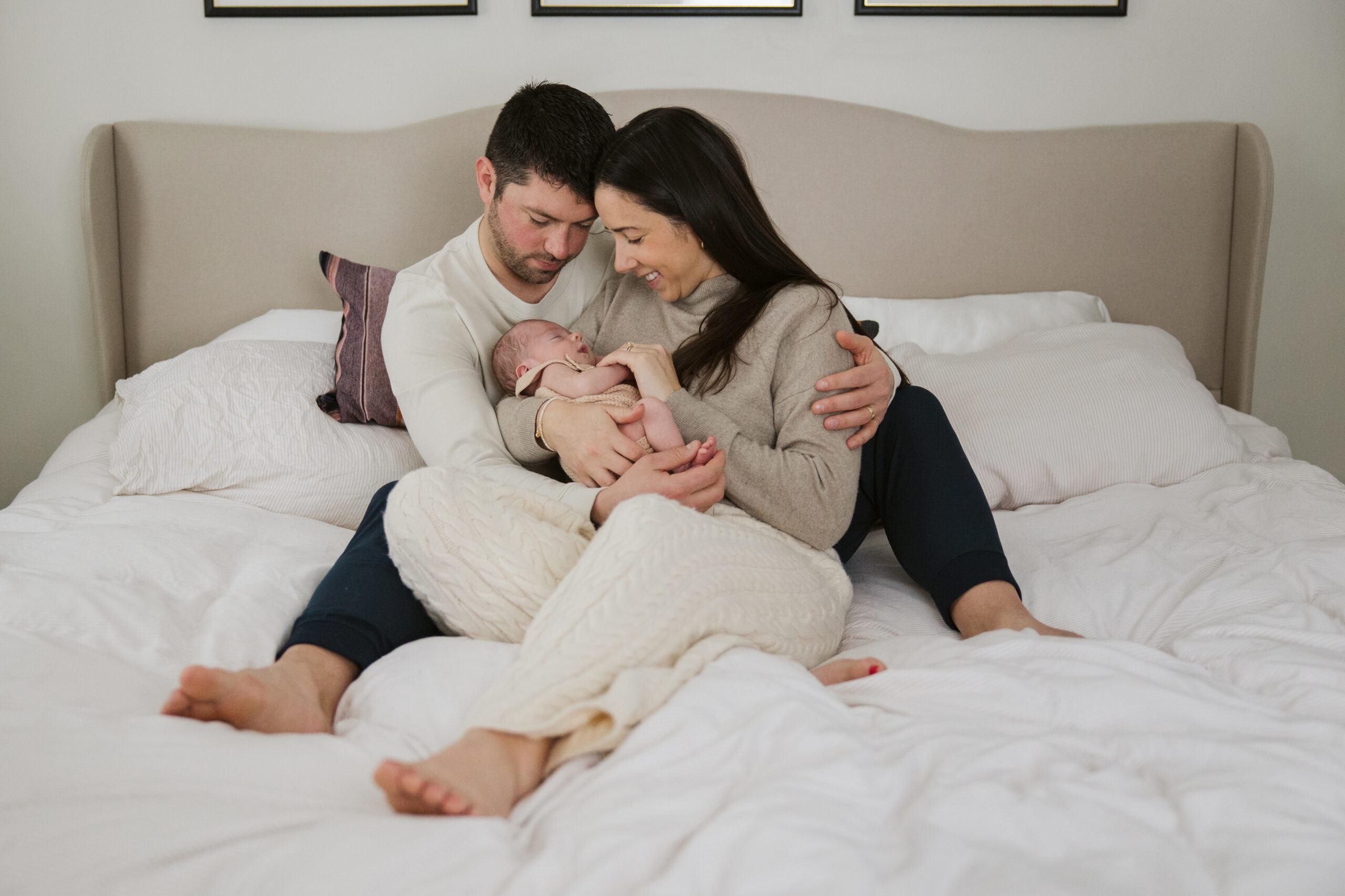 Traverse-city-michigan-newborn-photographer husband and wife sitting on bed during newborn family photos in traverse city