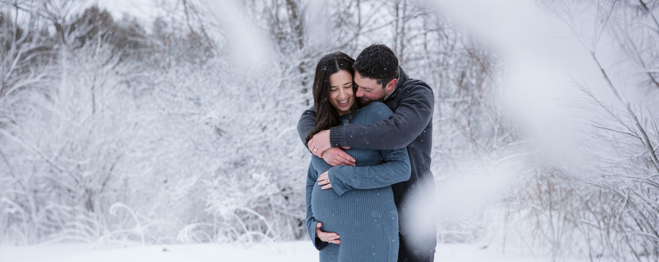 man and woman in the snow during winter maternity photos in traverse city michigan