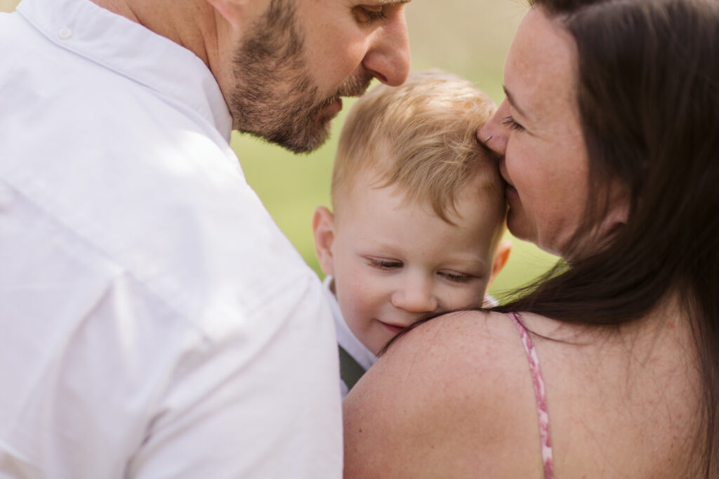 couple kissing little boy during blossoms in empire michigan family session